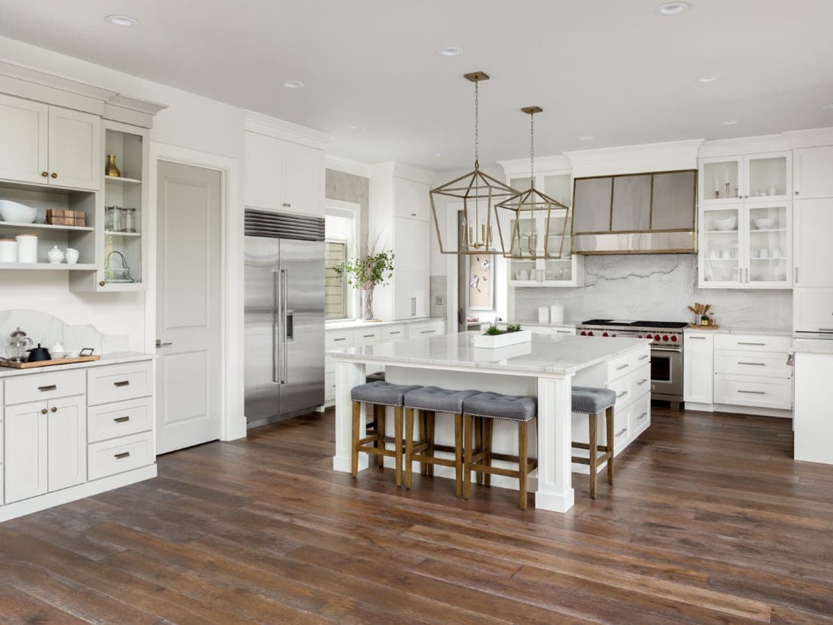 Wide white kitchen with a marble island and dark wide-plank hardwood running underneath